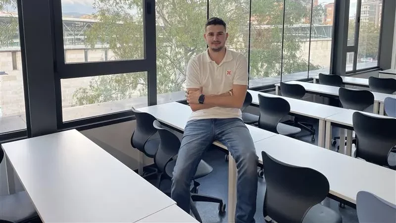 Estudiant del Grau en Gestió i Digitalització a l'Esport d'Euncet Business School assegut en una taula dins d'una aula amb finestres panoràmiques.