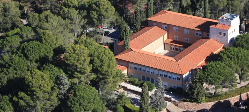 Vista aèria d´un campus envoltat d´arbres, amb edificis de sostres vermells en un entorn natural.