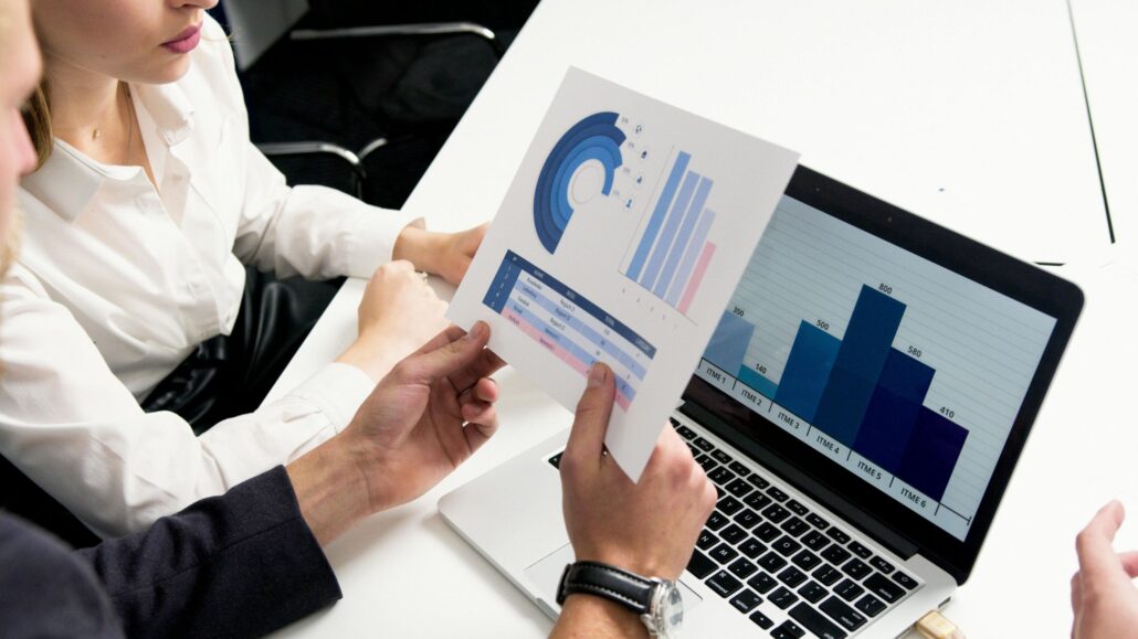 Personas analizando gráficos y datos financieros impresos y en una computadora portátil durante una reunión de trabajo