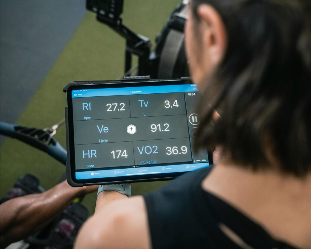 Persona observando una tablet que muestra datos biométricos como frecuencia cardíaca, volumen respiratorio y consumo de oxígeno durante el ejercicio.