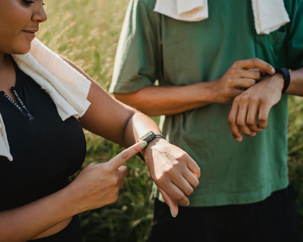 Mujer y hombre revisando sus relojes deportivos después de una sesión de entrenamiento en la naturaleza.