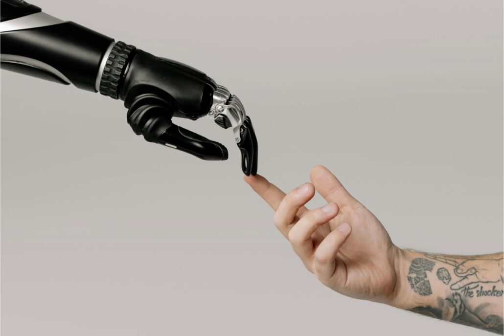 Una mano humana tatuada tocando la punta de un dedo robótico en un gesto de conexión simbólica entre humanidad y tecnología