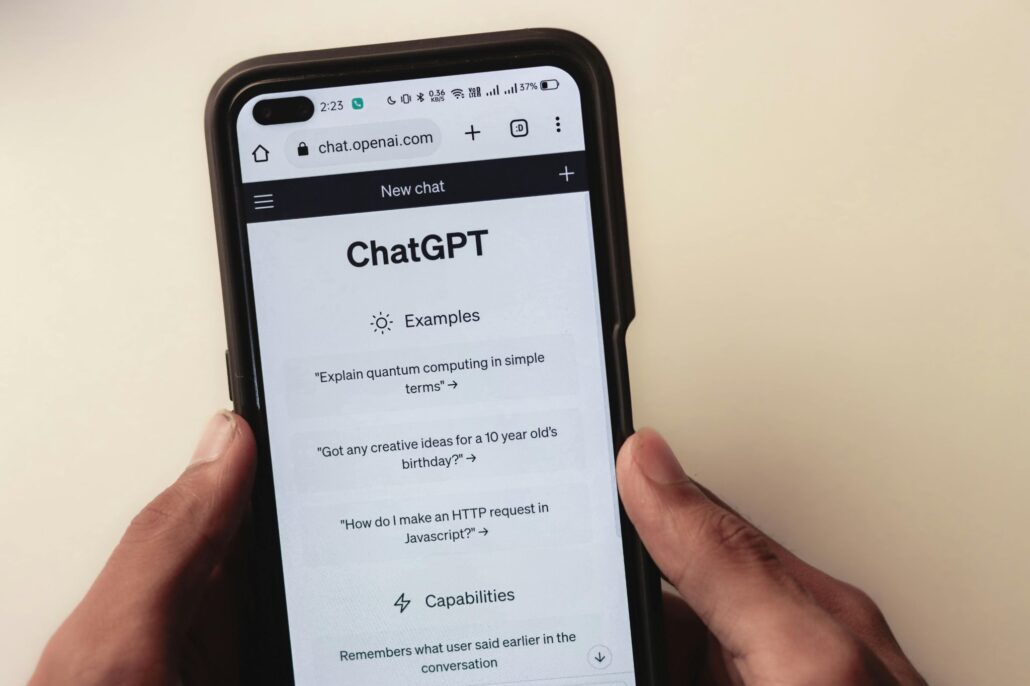 Persona sosteniendo un teléfono móvil con la página web de ChatGPT abierta, mostrando ejemplos de uso de la inteligencia artificial