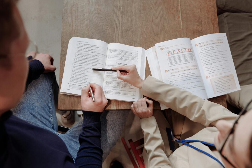 Personas estudiando juntas con libros abiertos sobre una mesa de madera.